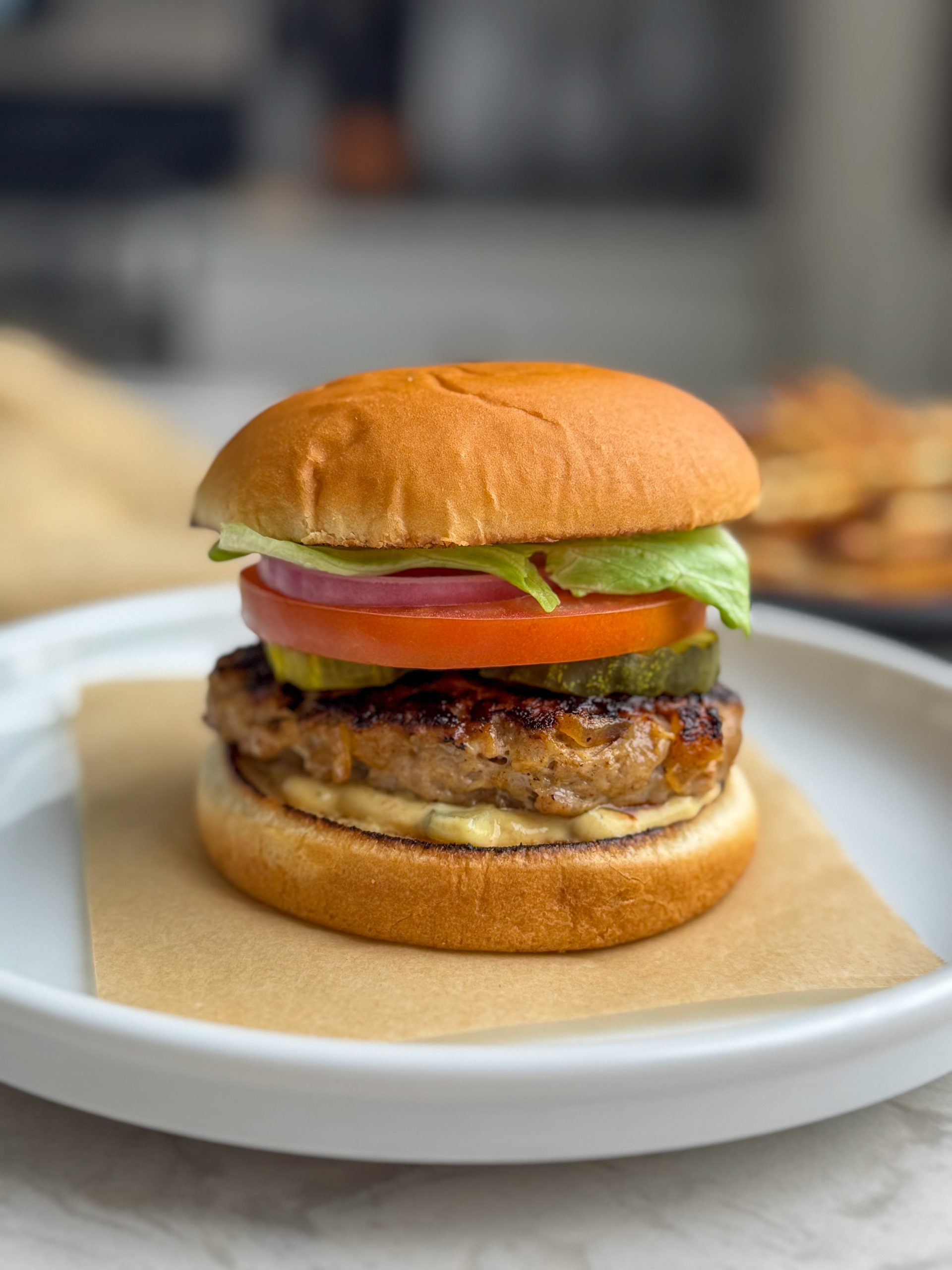 Chicken burger on a white bun with sauce, pickles, tomato, red onion and lettuce.