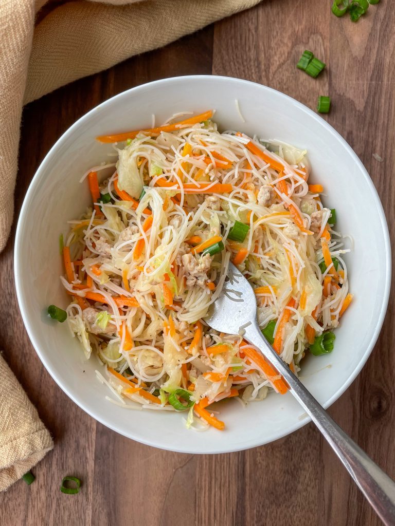 Egg roll in a bowl with a fork and green onion sprinkled on top.