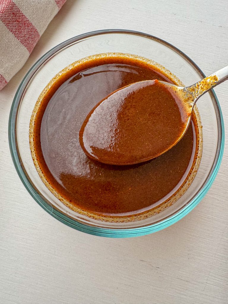 Quick and easy homemade red enchilada sauce in a glass bowl with a spoon.