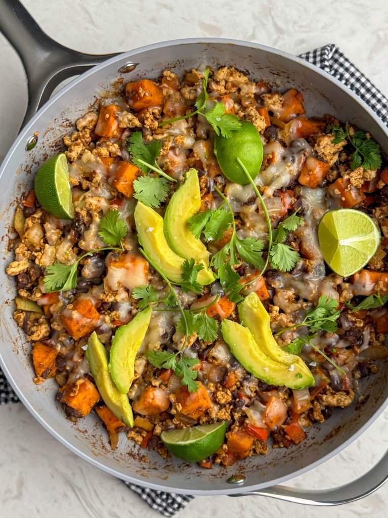 Ground turkey and sweet potato taco skillet in a large pan with cilantro, limes and avocado.