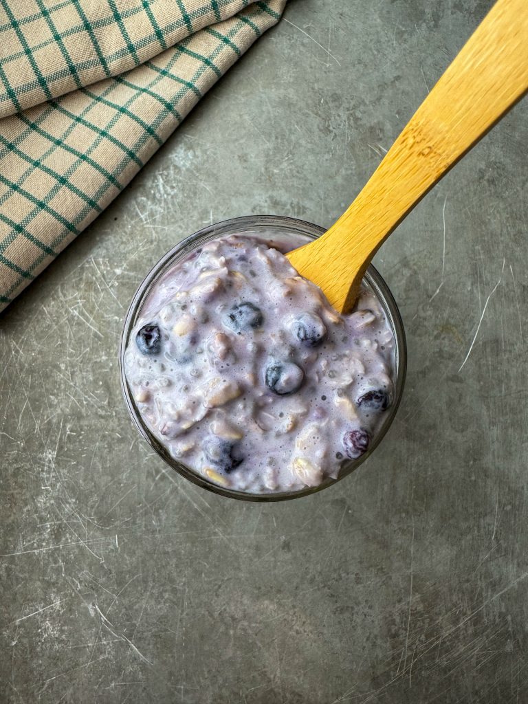 Easy blueberry protein overnight oats in a small mason jar with wooden spoon and kitchen towel in the background.