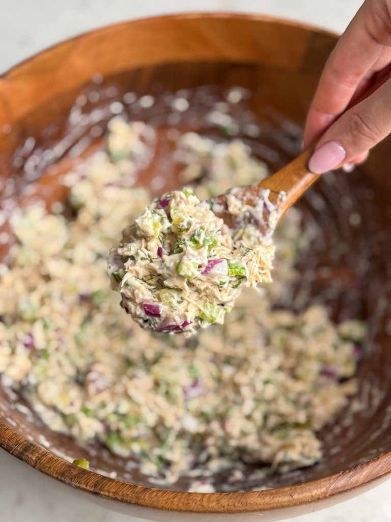 Hand holding a wooden spoon with tuna salad.