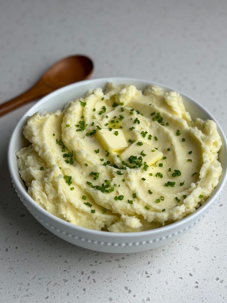 White bowl of mashed potatoes with butter and chives.