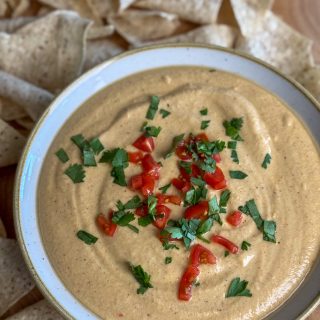 High protein cottage cheese queso topped with tomatoes, cilantro with tortilla chips in the background.