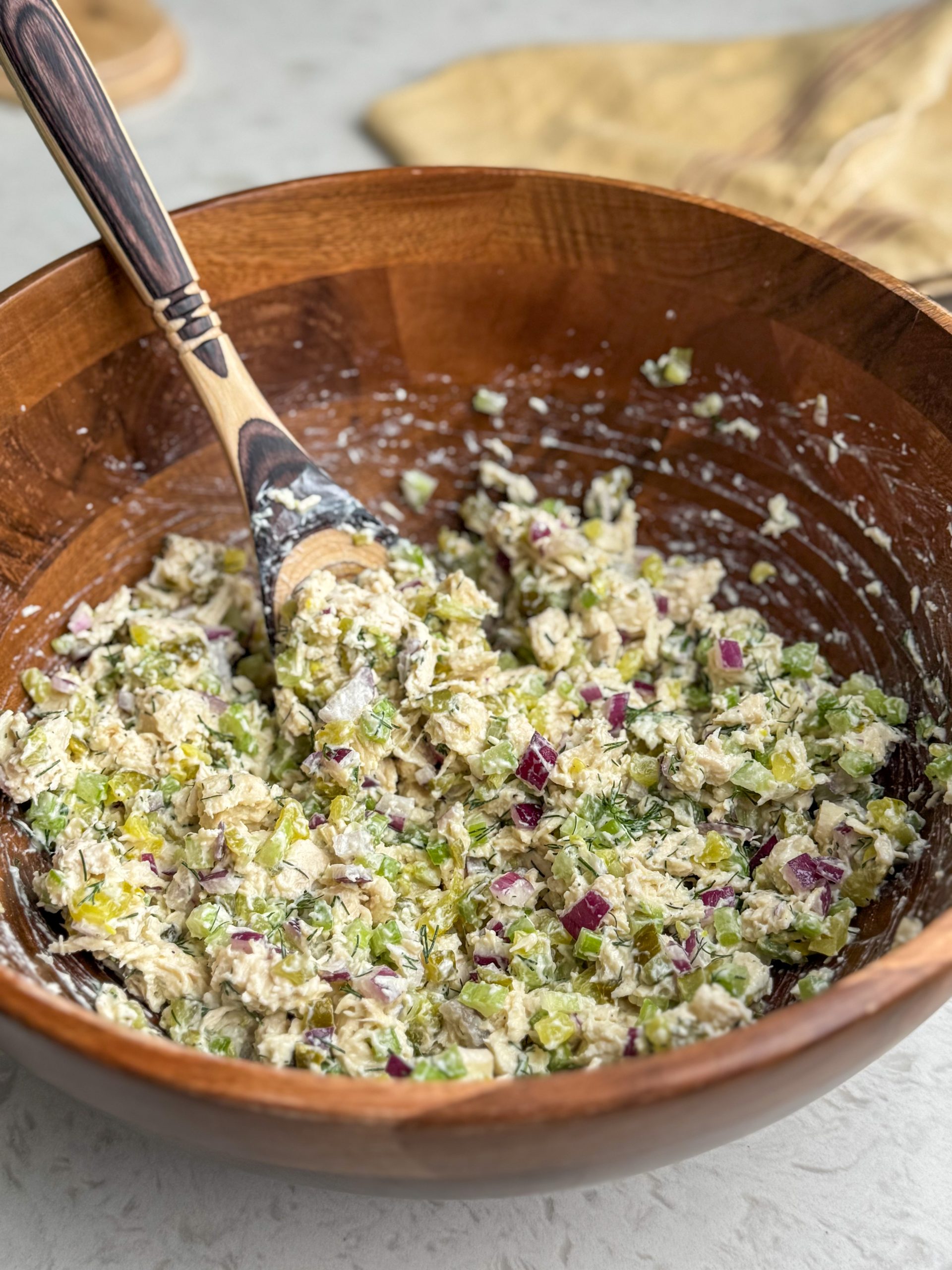 Large wooden bowl full of dill pickle chicken salad with a wooden spoon.