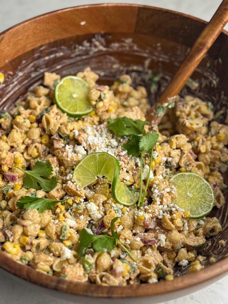High protein elote pasta salad with chicken, limes and cilantro in a large wooden bowl.