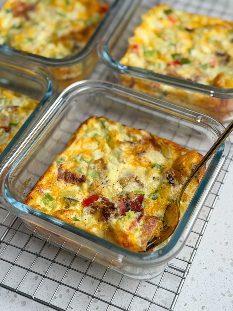 Bacon cheddar breakfast casseroles in glass dishes with a gold fork.