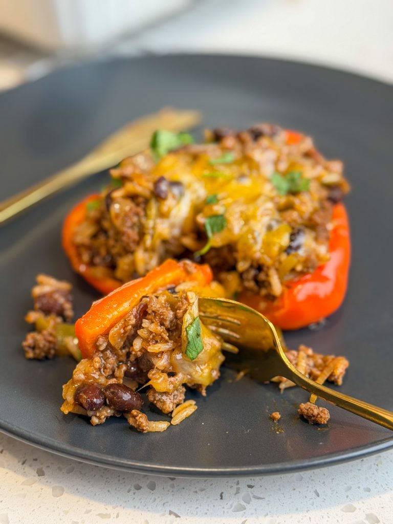 Taco stuffed pepper with cheese on a gray plate with a fork holding a bite.