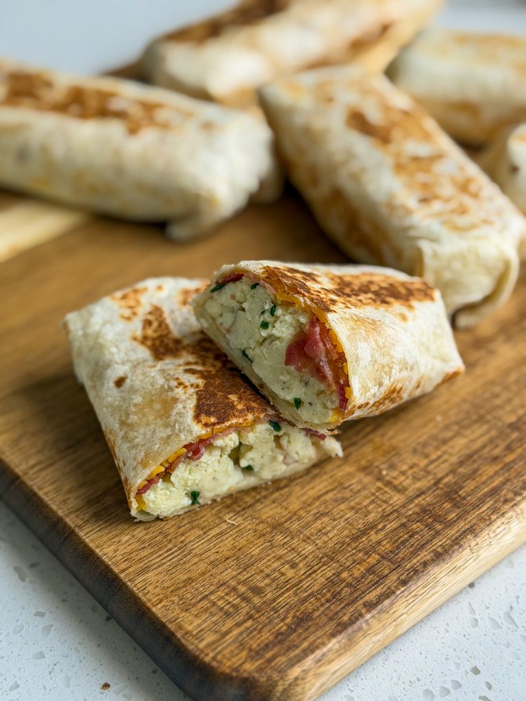 Bacon egg and cheddar breakfast wraps on a brown wooden cutting board.