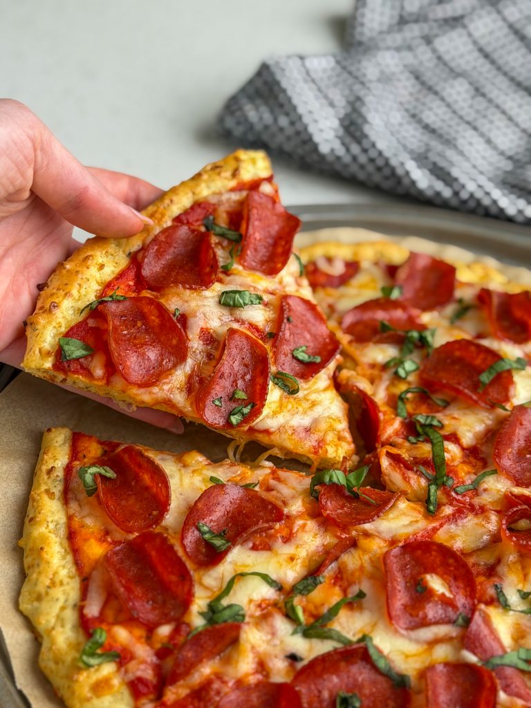 Hand holding a slice of pepperoni pizza with cottage cheese crust.