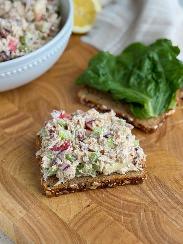 Apple and almond tuna salad on multigrain bread on a wooden cutting board.