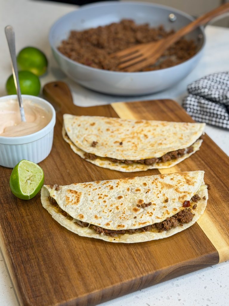 Chipotle lime beef quesadillas on a brown wooden cutting board with fresh limes.