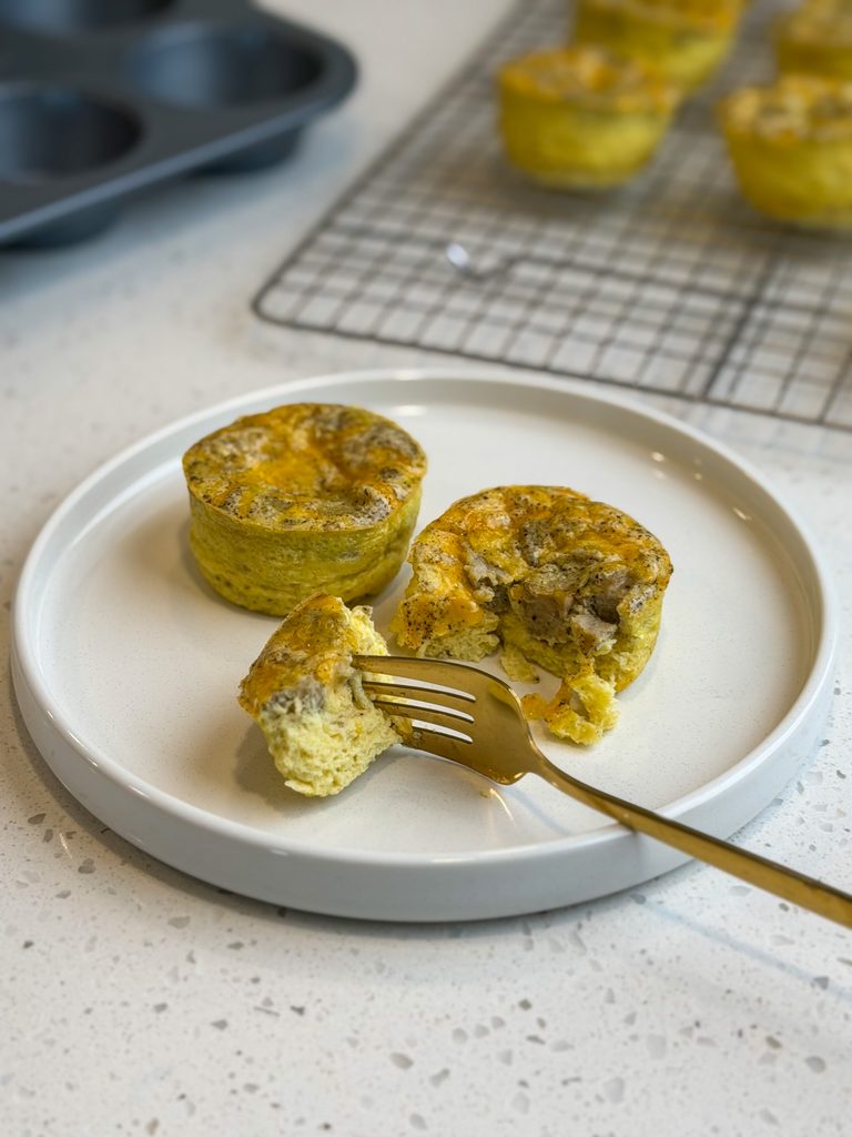 Gold fork with a bit of sausage and cheddar egg bite on a white plate.