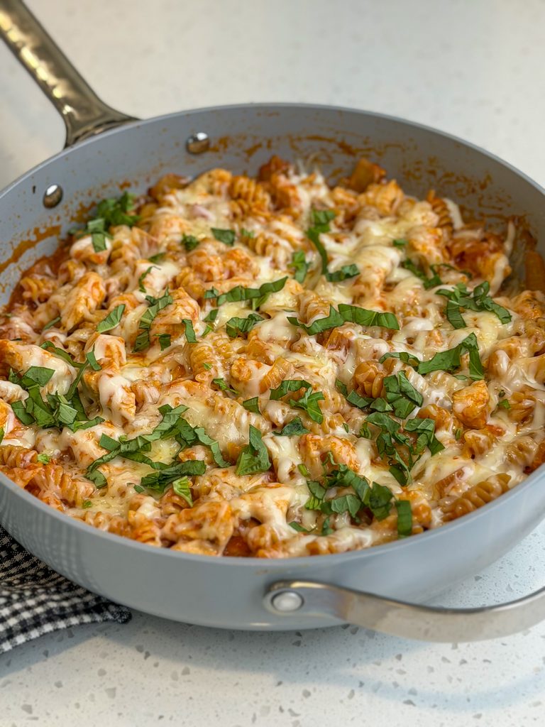 Easy one pan chicken parmesan pasta with cheese and fresh basil in a gray pan.